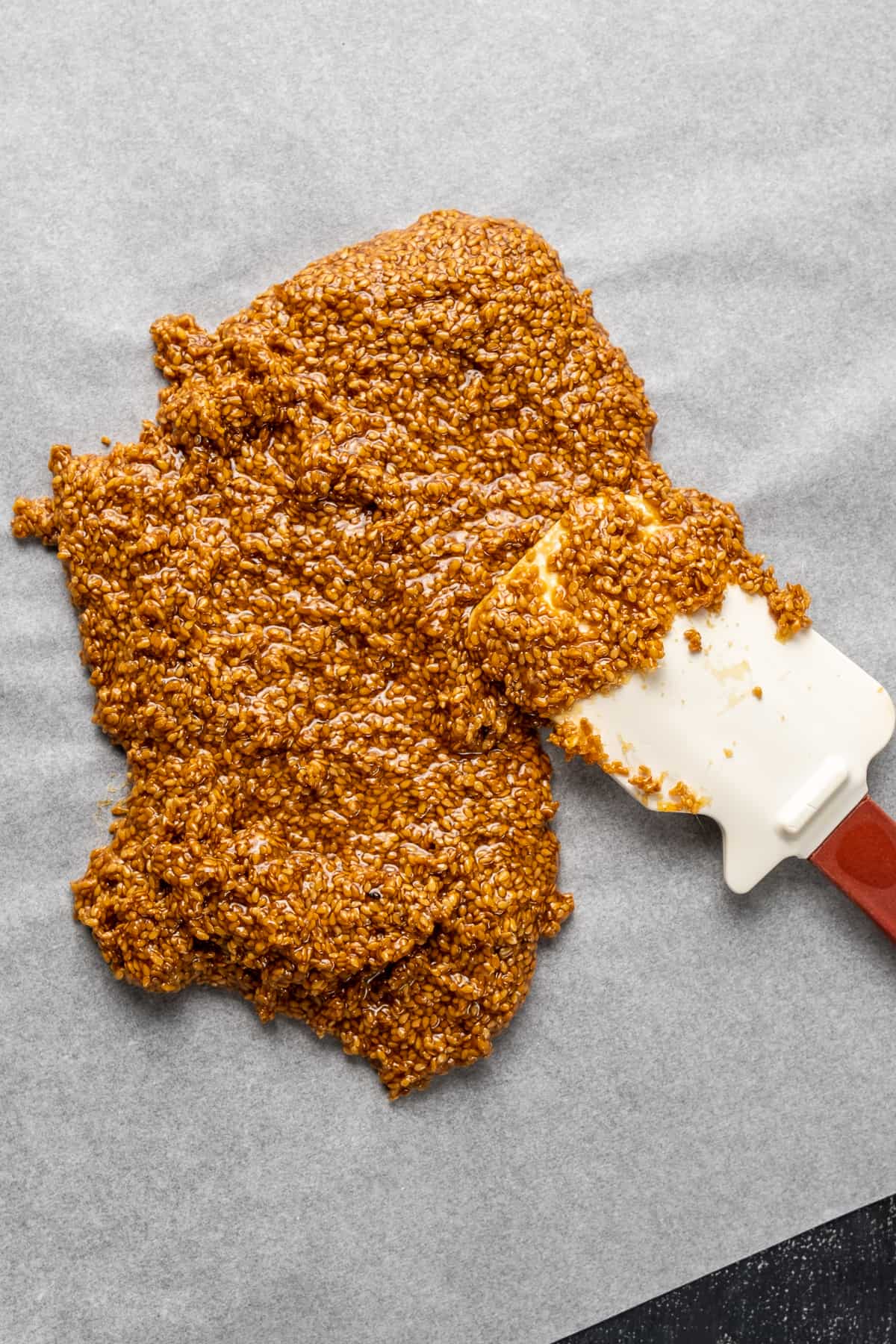 Spreading sesame seed and sugar mixture on a baking paper with a spatula.