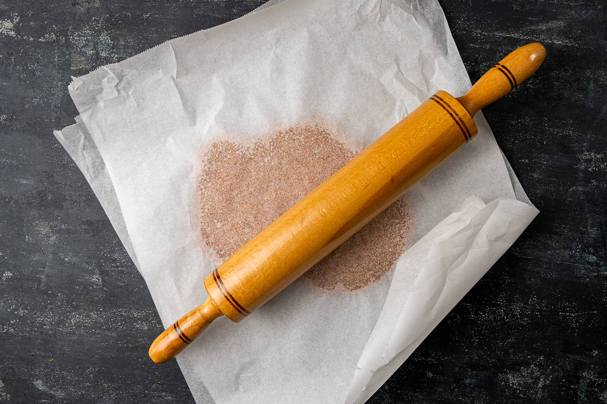 Sesame seed and sugar mixture between two layers of baking paper and a rolling paper on it.