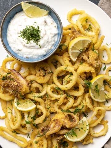 Calamari rings served with lemon slices and a sauce in a small bowl on the side.