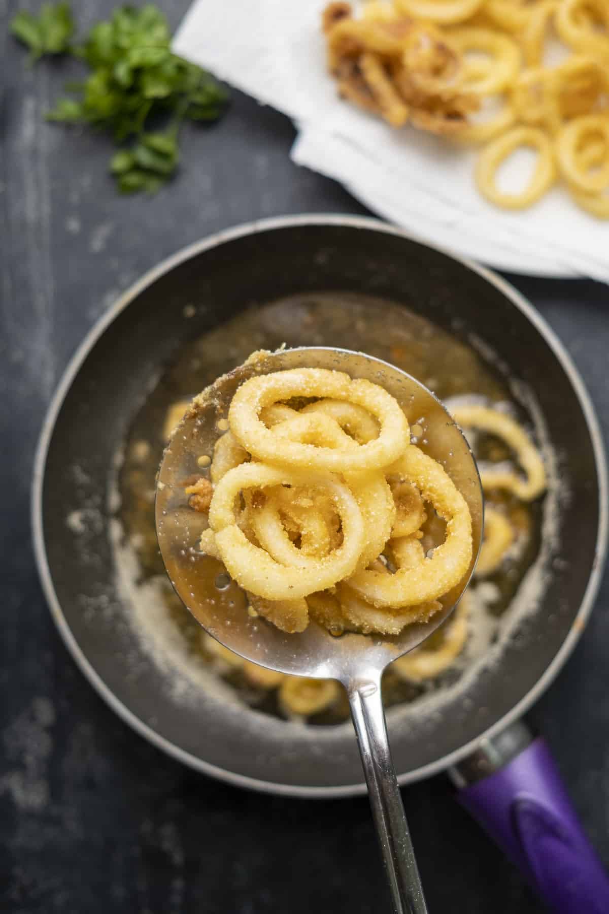 Removing fried calamari rings from hot oil with a slotted spoon.