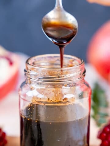 A spoon pouring pomegranate molasses into a jar.