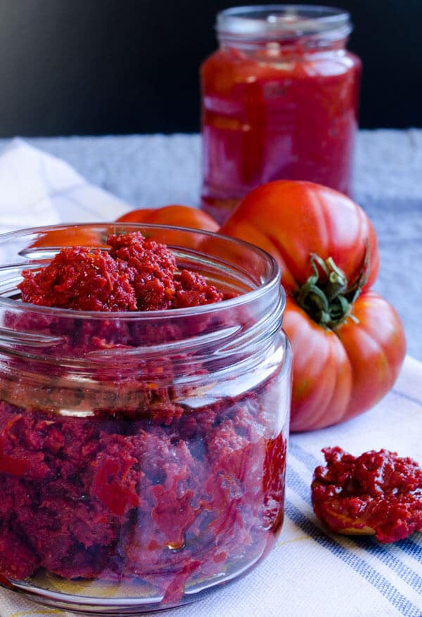 Fresh tomato paste in a jar and fresh tomatoes on a kitchen towel. 