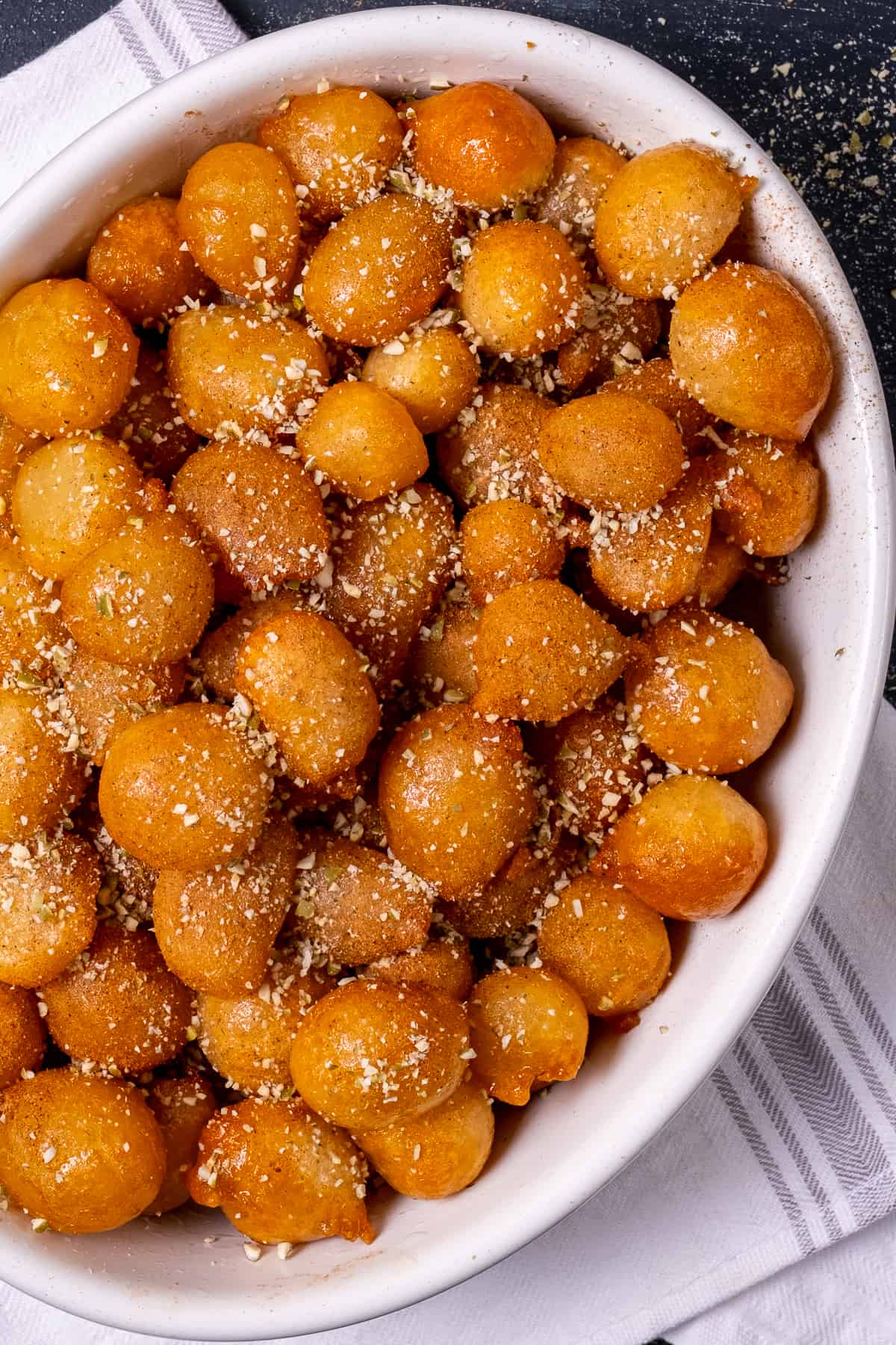 Lokma pastry dusted with powdered cinnamon and crumbled walnuts in a white oval bowl.