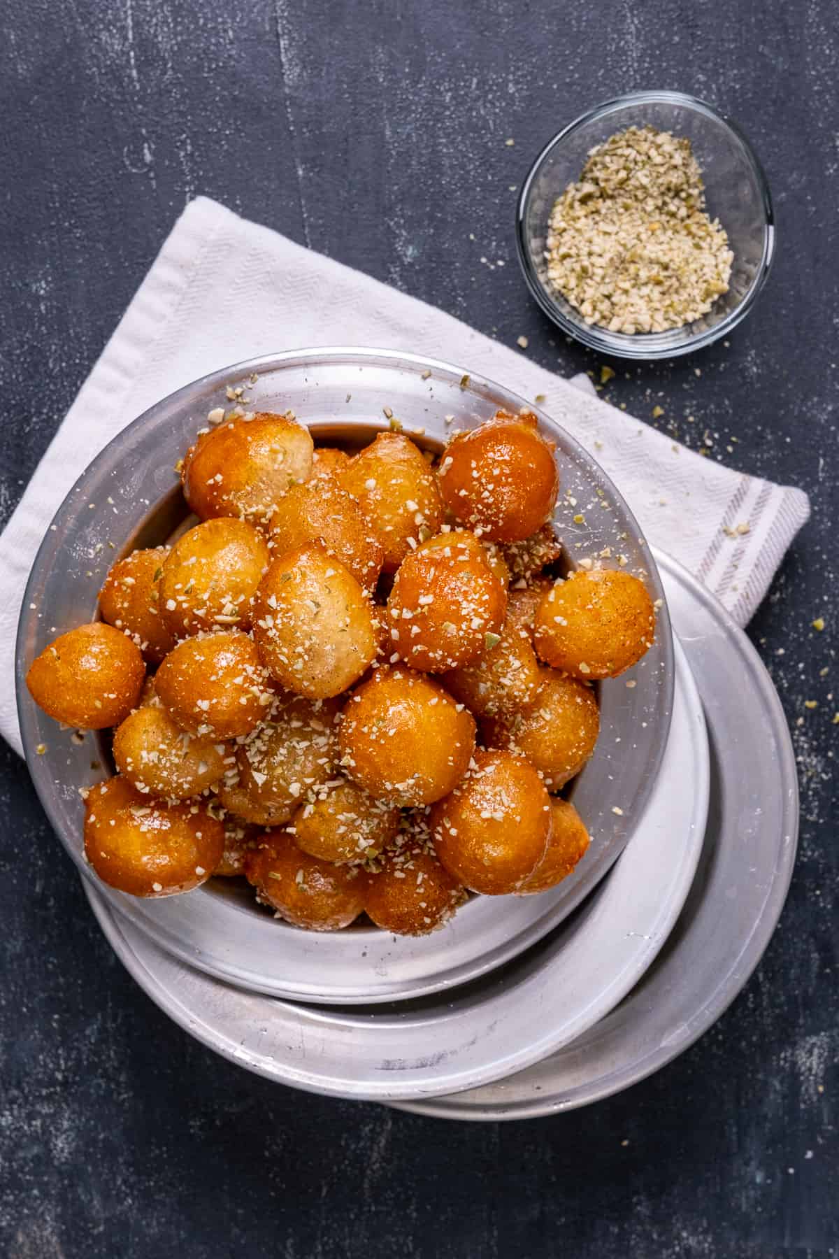Fried sweet balls garnished with crumbled walnuts on a metal plate.