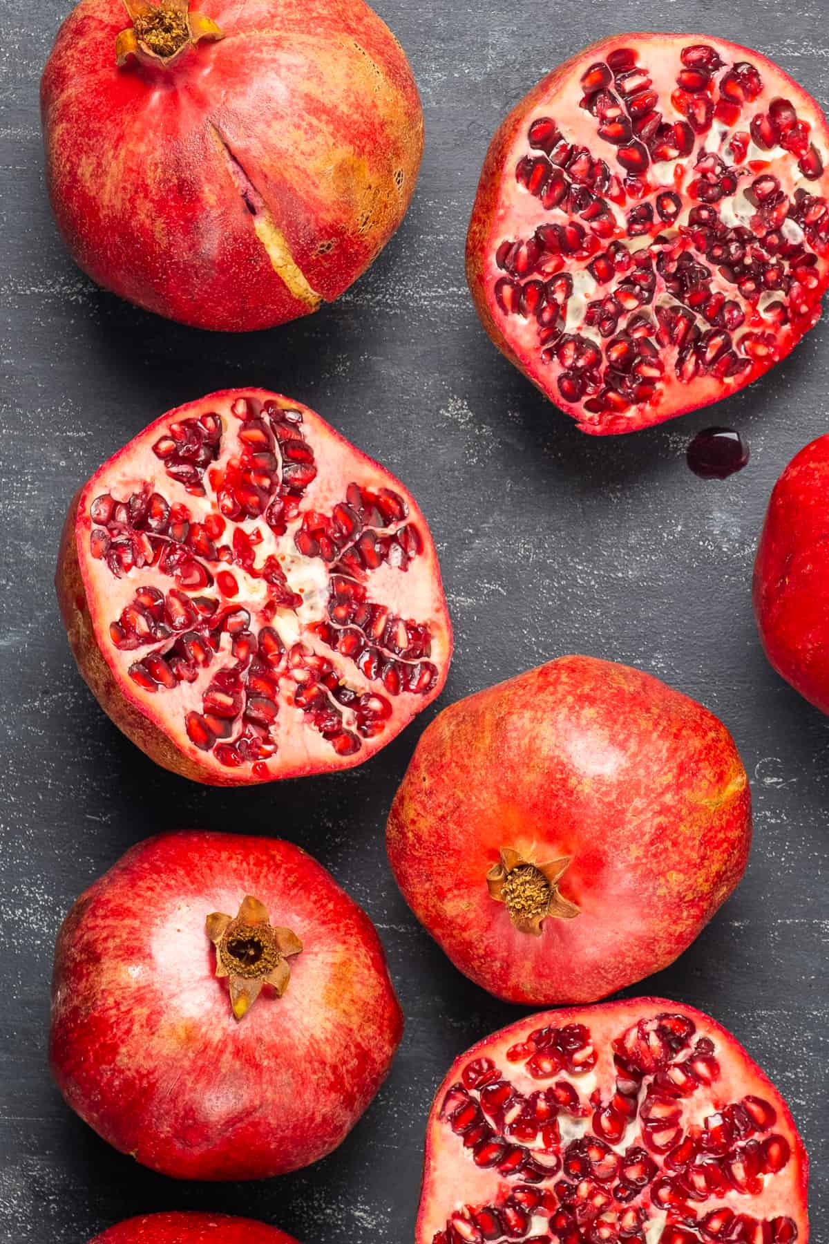 Whole pomegranate fruit, some halved on a dark background.