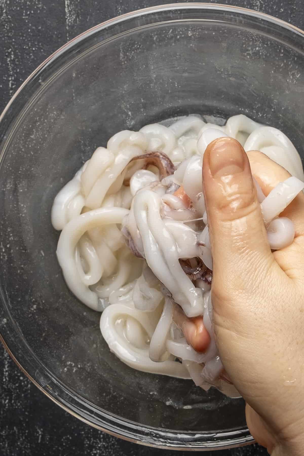 A hand massaging squid rings with lemon juice and baking soda.