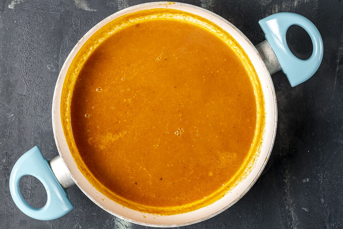 Blended tomato soup with carrot and onion in a pan on a dark background.