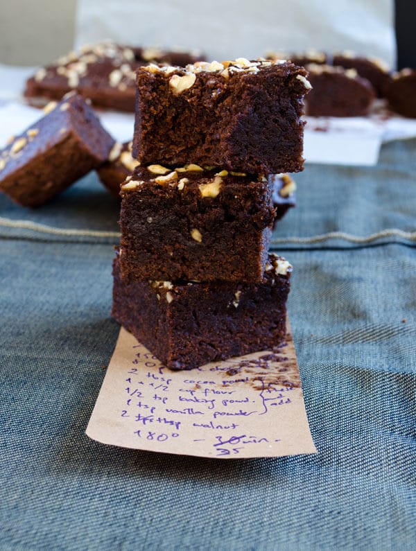 Chocolate and apple brownies stacked on a piece of paper with a recipe note