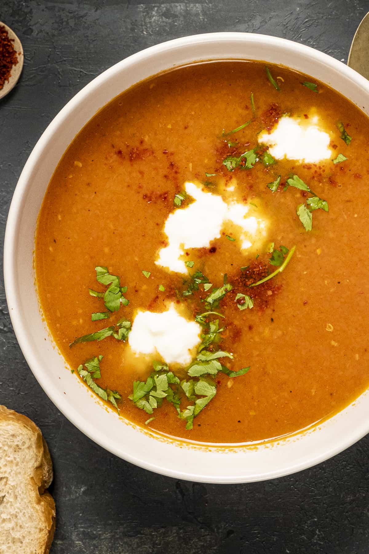 Carrot and tomato soup garnished with yogurt and parsley in a white bowl.