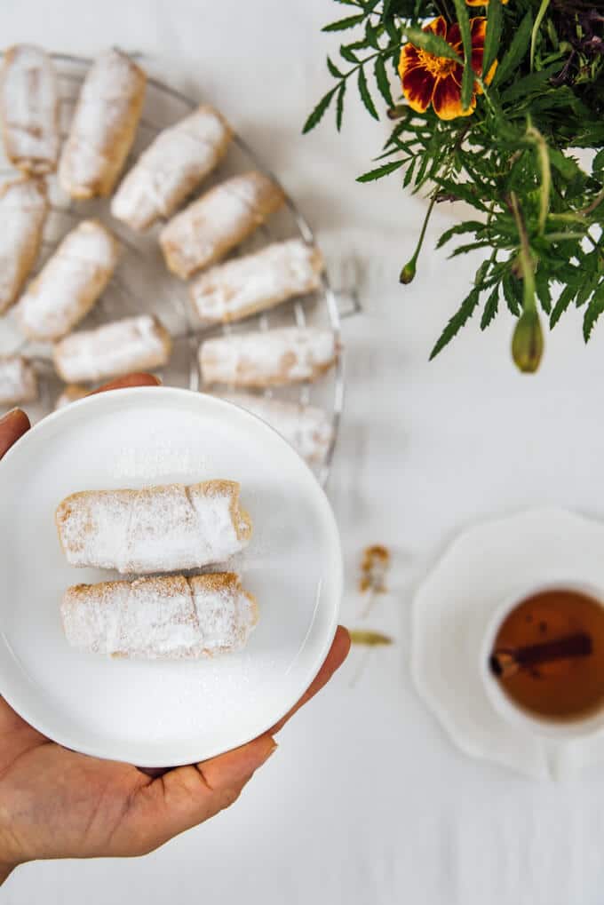 Hands holding Turkish apple cookies on a small white plate , a cup of tea is on the side.
