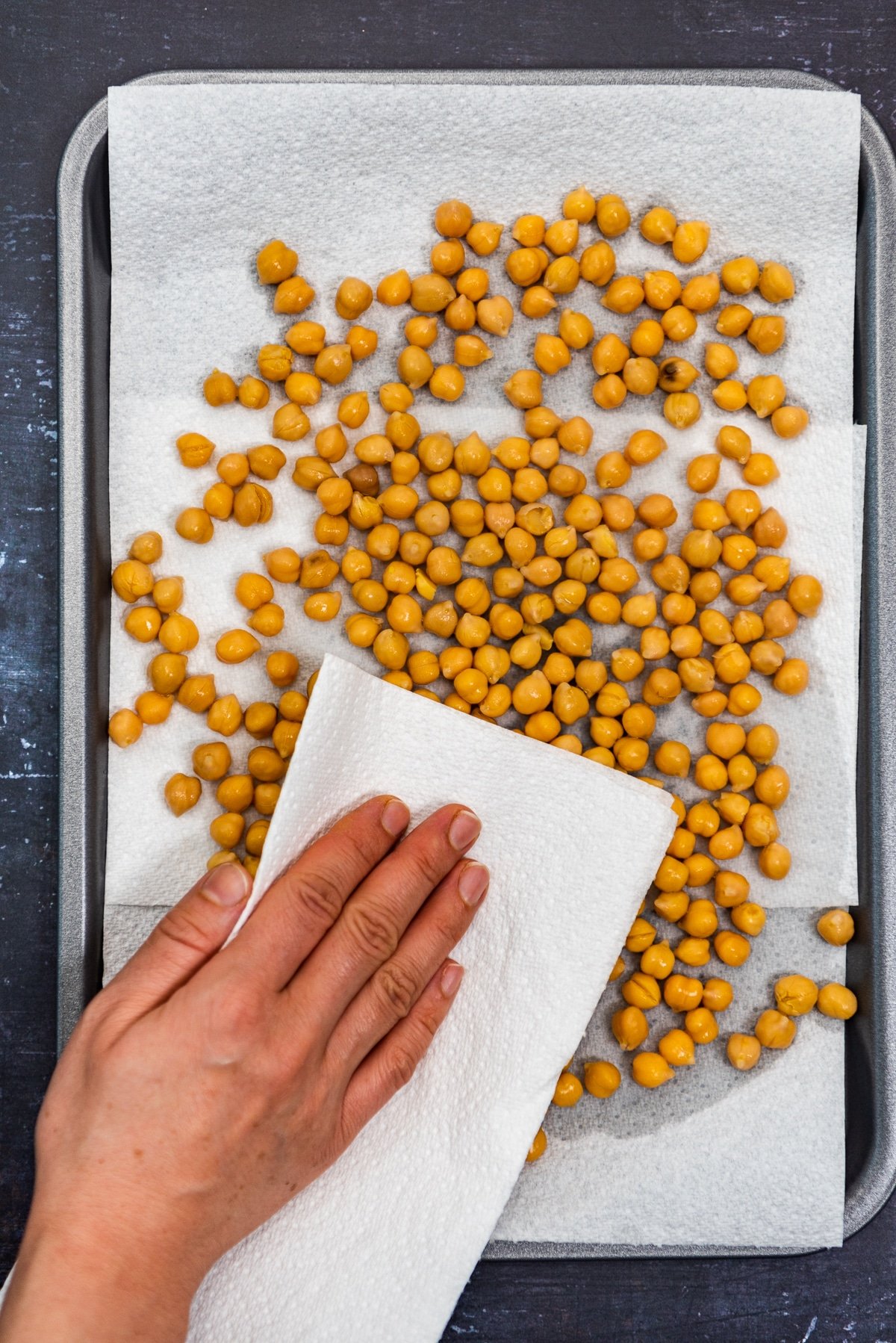 A hand drying cooked chickpeas on a baking sheet with paper towel.