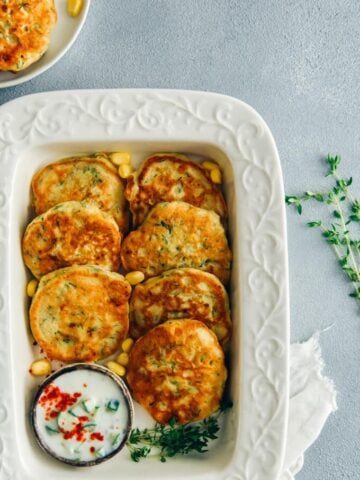 Avocado corn fritters with a yogurt sauce on the side in a white baking dish