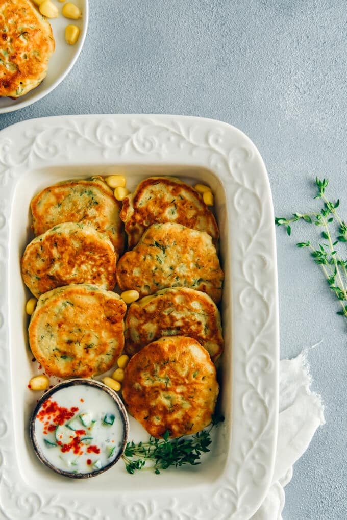 Avocado Corn Fritters served with yogurt dip make a wonderful appetizer for summer get-togethers. Packed with avocado, fresh corn and feta, these restaurant- style fritters are so addictive. They make a great after-school snack too! #cornfritters #avocadofritters #glutenfreefritters #afterschoolsnack Avocado corn fritters with a yogurt sauce on the side in a white baking dish