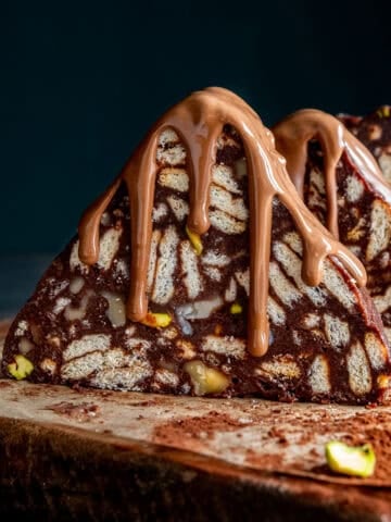 Close-up of Turkish Mosaic Cake slices shaped like triangular prisms, topped with melted milk chocolate, served on a wooden board.