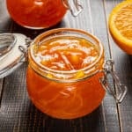 Orange jam in glass jars and a slice of orange on the side.