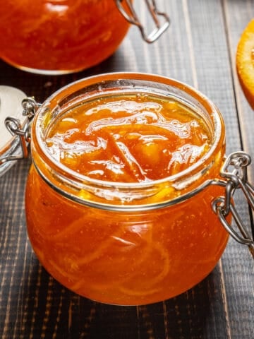 Orange jam in glass jars and a slice of orange on the side.