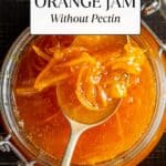 Orange jam in a glass jar and a spoon inside.