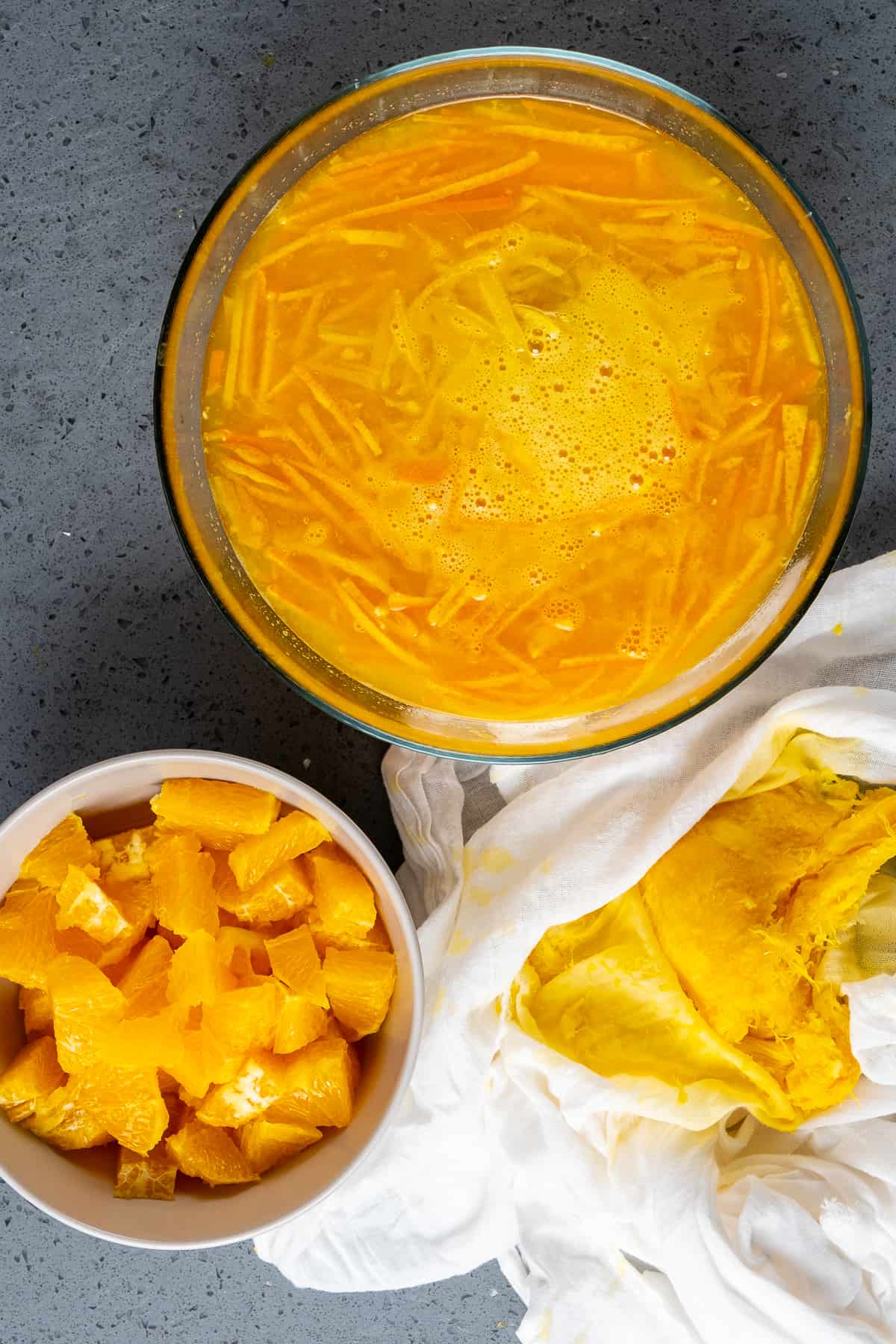 Chopped oranges in a bowl, orange juice and zest slices in another bowl.
