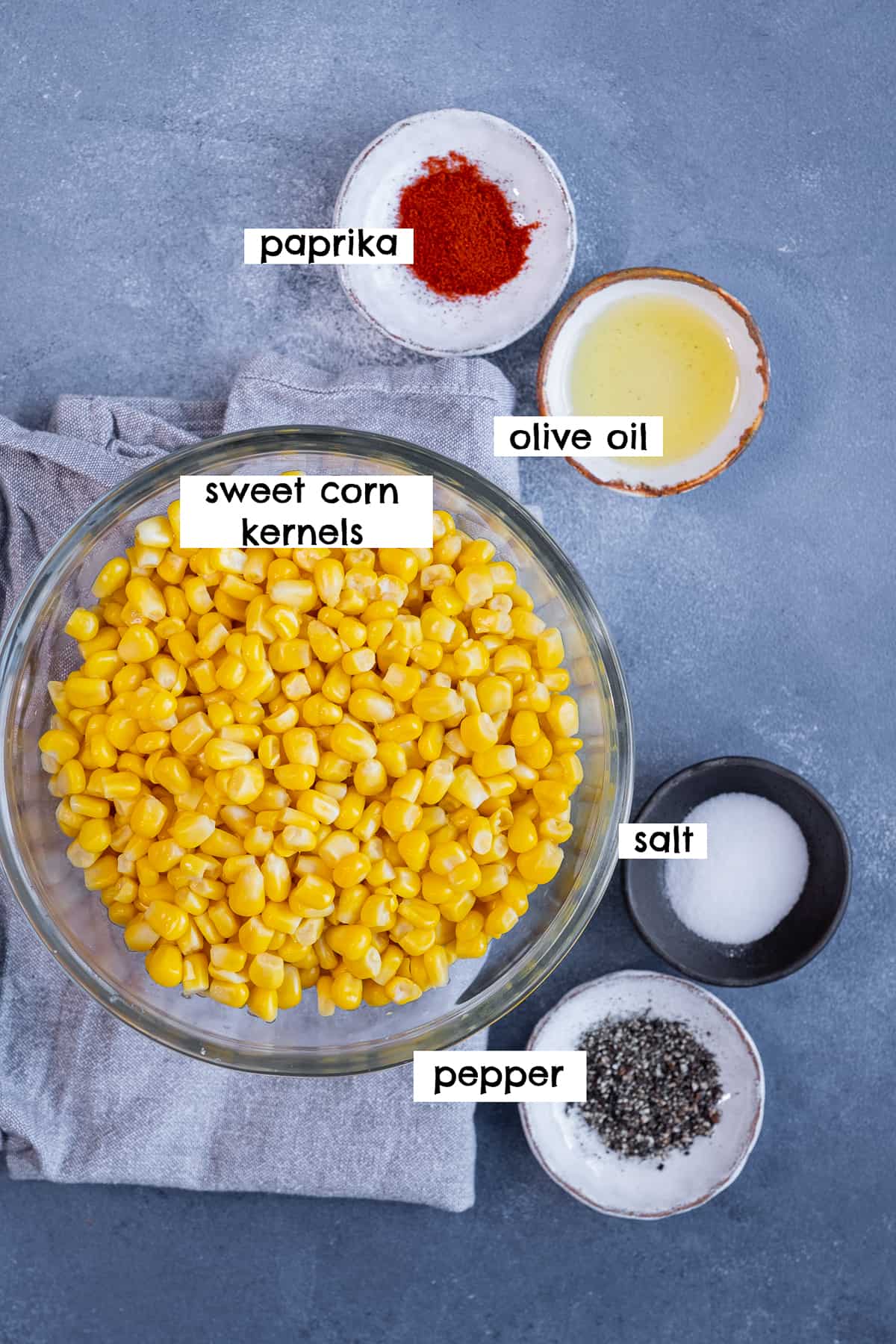 Sweet corn kernels, paprika, oil, salt and pepper on a grey background.