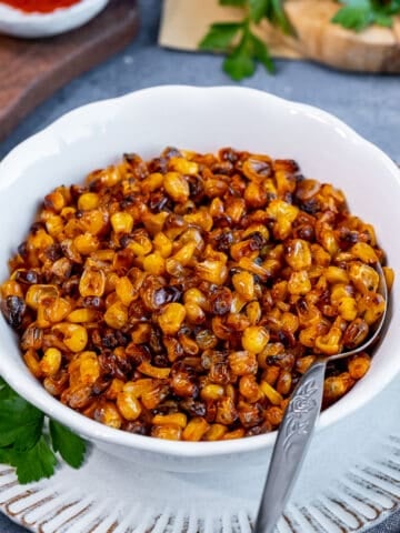 Roasted corn kernels in a white bowl and a spoon inside it.