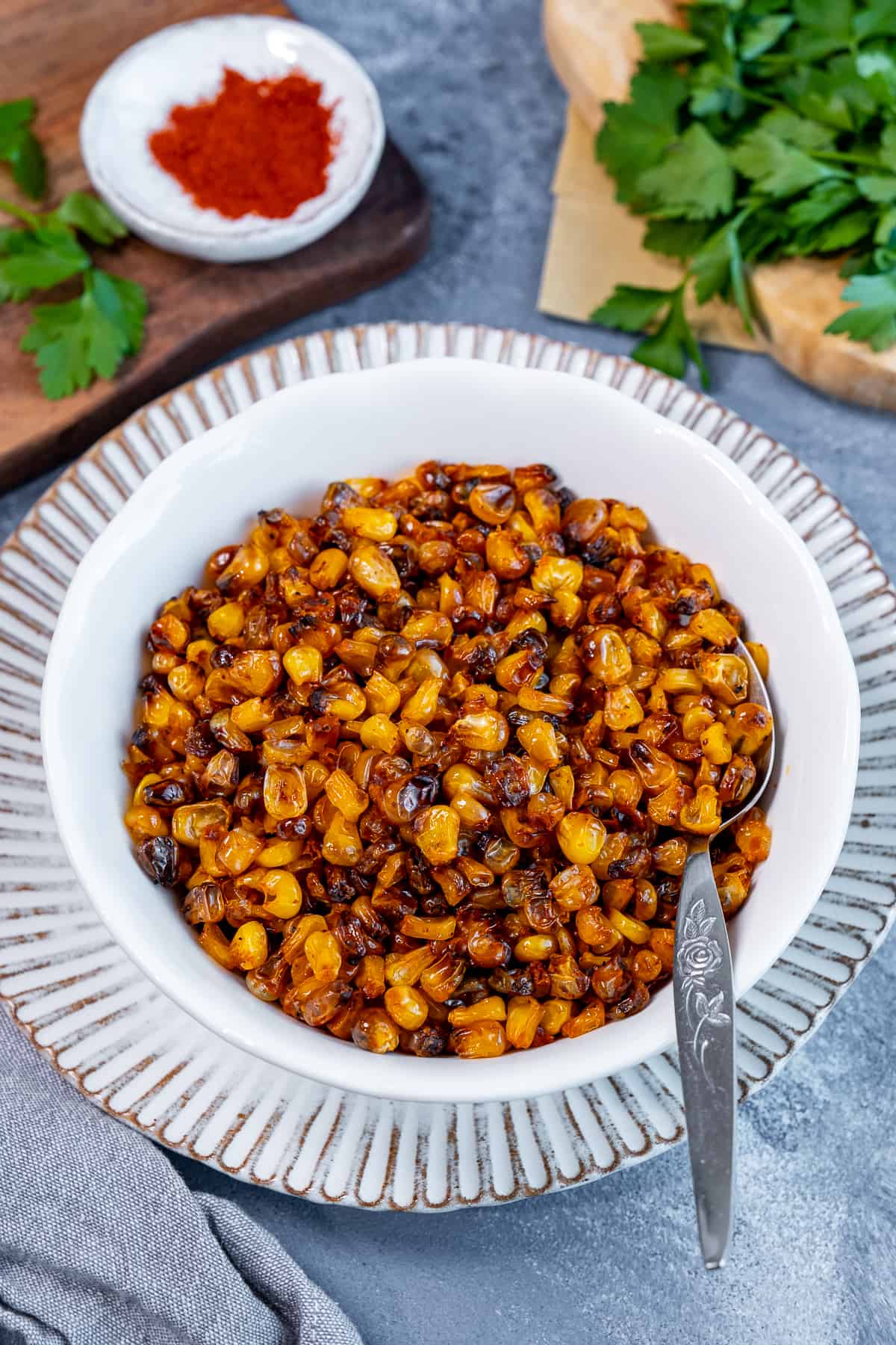 Roasted corn kernels in a white bowl, paprika and parsley on the side.