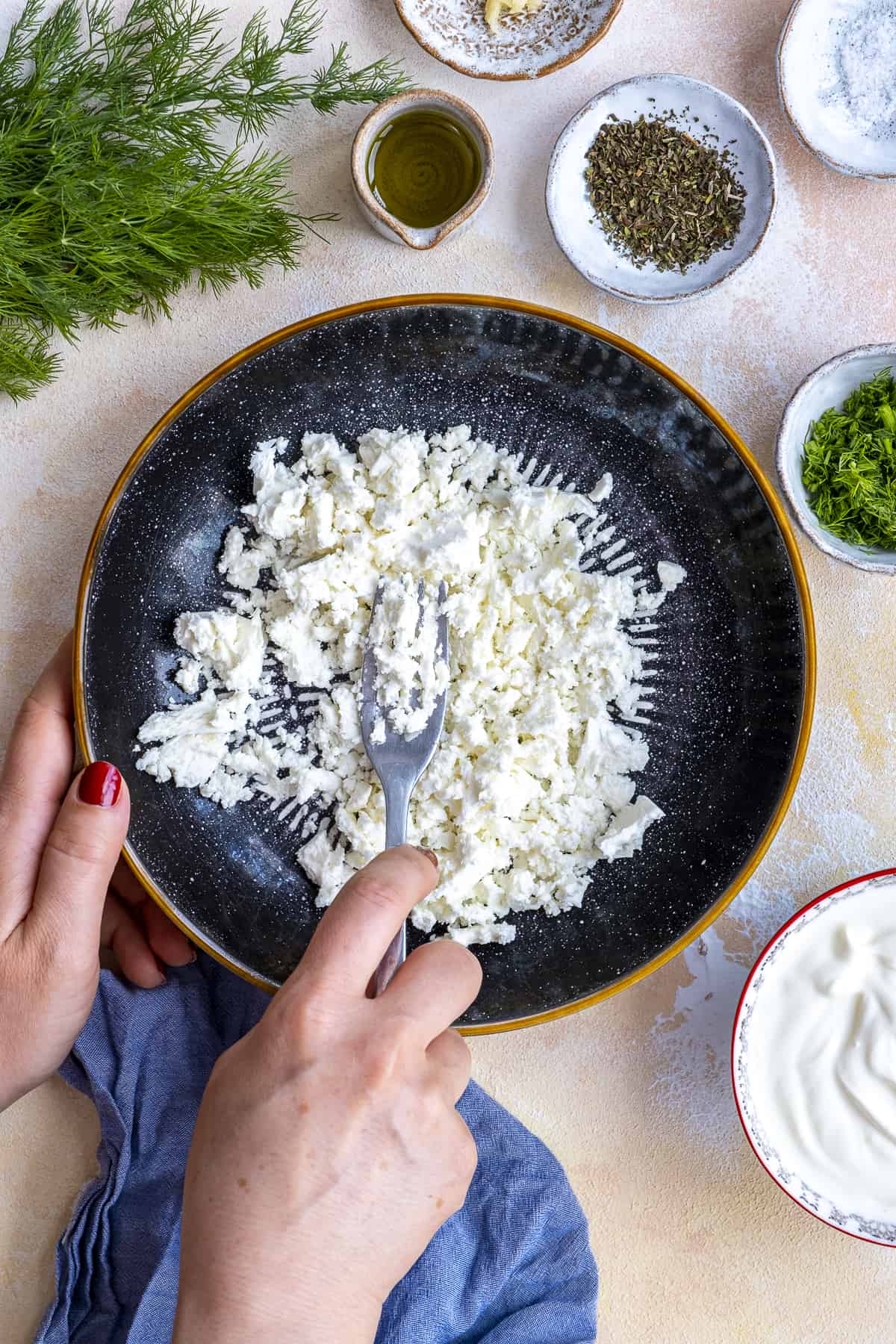 Woman hands mashing feta cheese with a fork in a black bowl.
