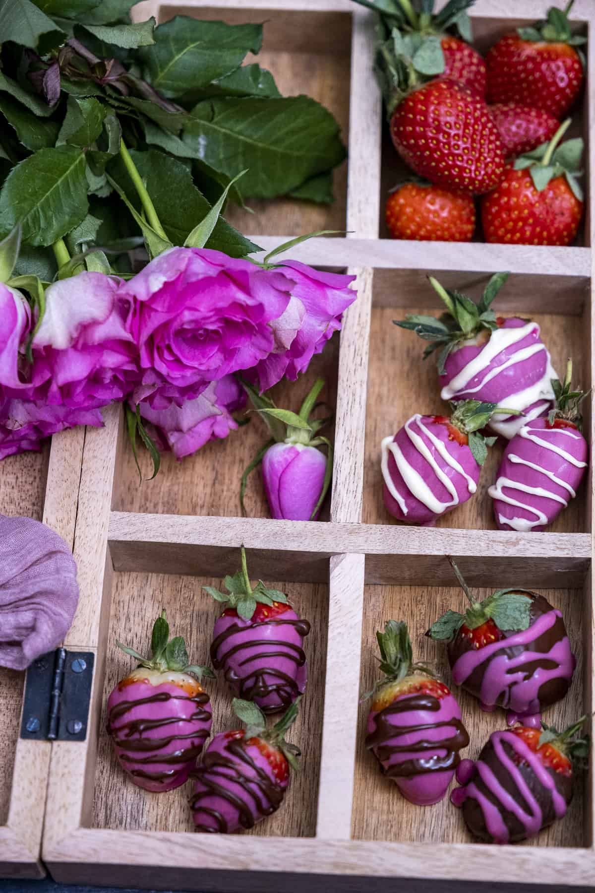 Pink strawberries with dark and white chocolate drizzles, pink roses and red strawberries in a wooden box.