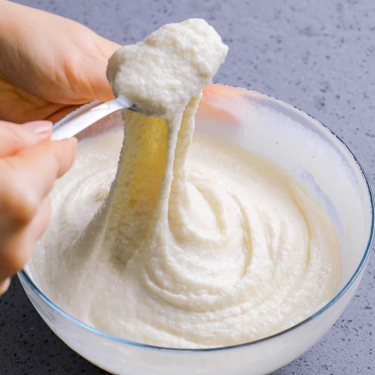 Hands churning ice cream with a fork and showing how stretchy it is.