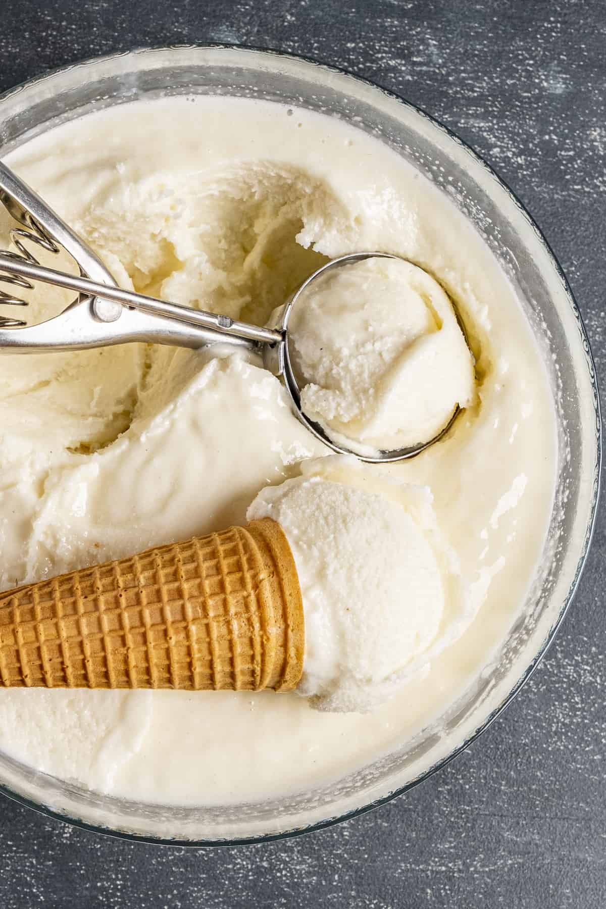 Ice cream in a large bowl, a cone and a scoop inside it.