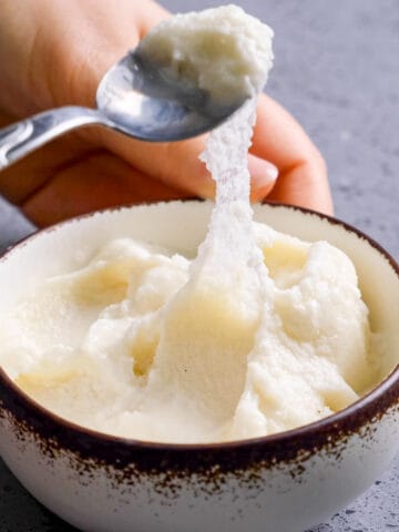 Hands holding a bowl and showing how stretchy the ice cream is with a spoon.