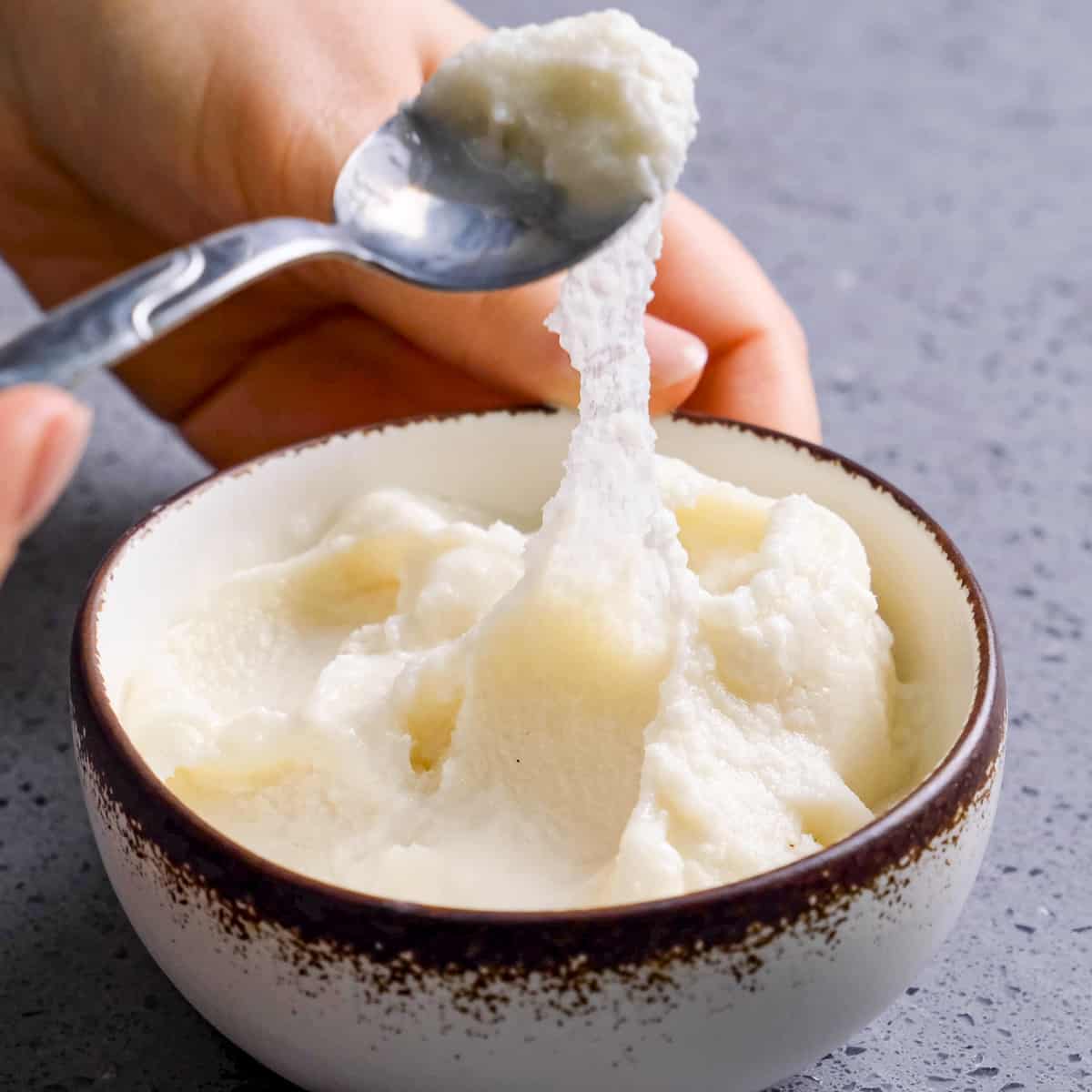 Hands holding a bowl and showing how stretchy the ice cream is with a spoon.