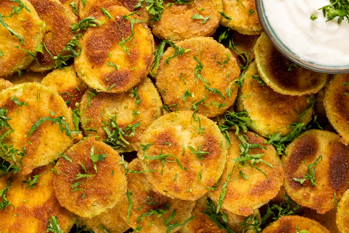 Close shot of breaded zucchini chips garnished with chopped parsley.