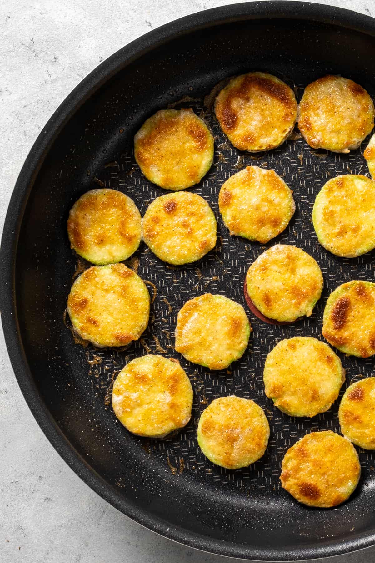 Breaded zucchini slices fried in a non-stick pan.