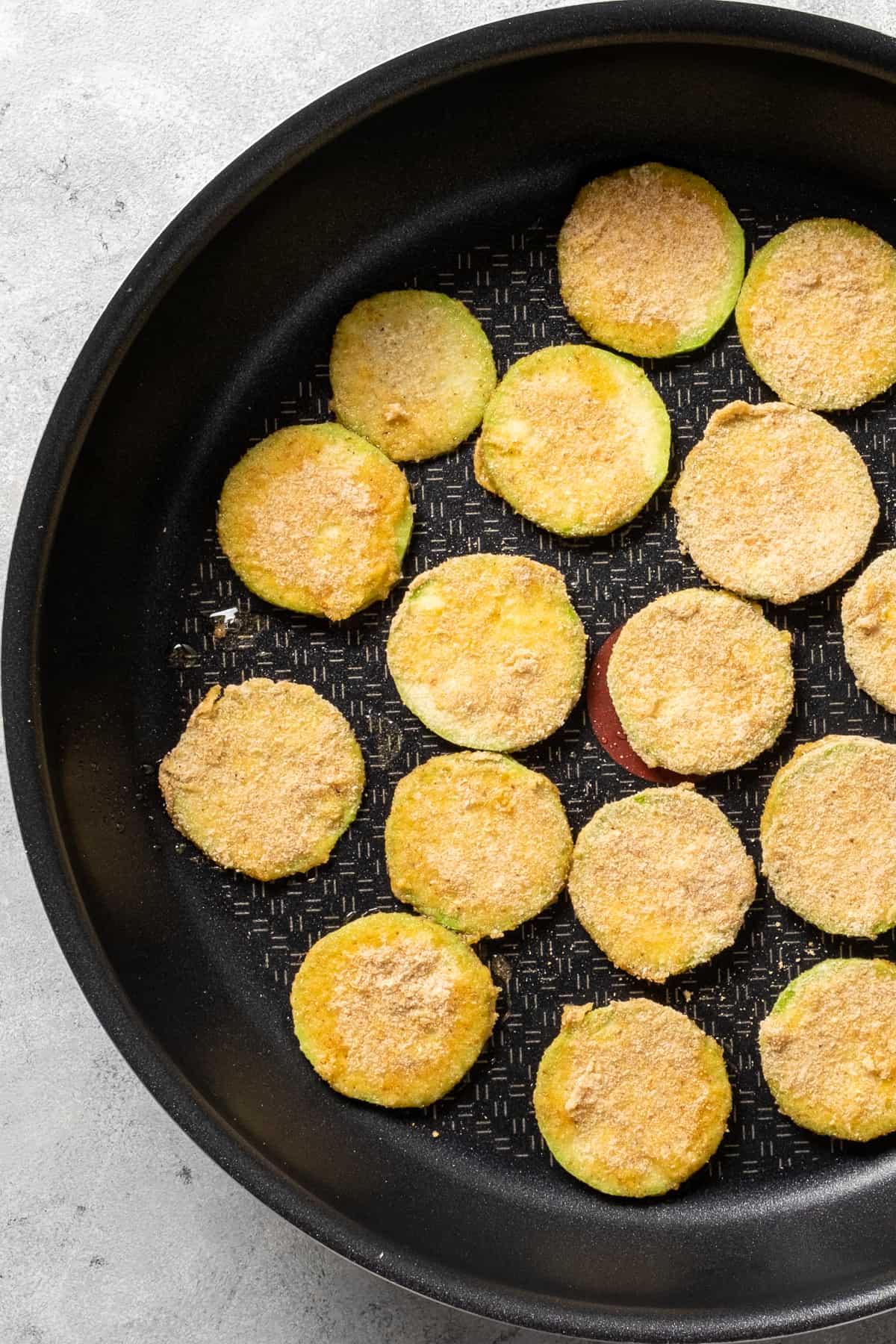 Breaded zucchini slices frying in a non-stick pan.