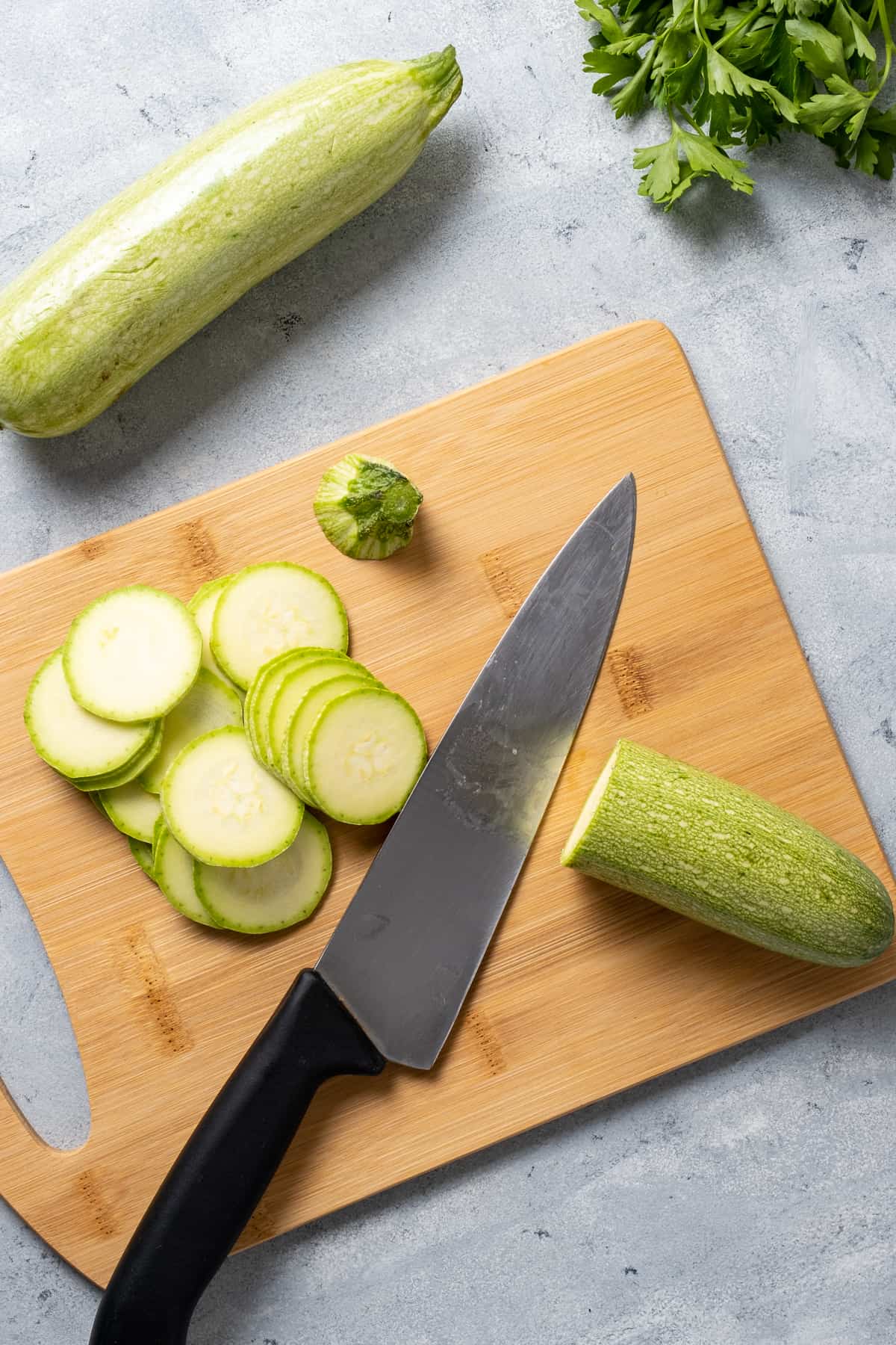 Sliced zucchini and a knife on a wooden cutting board.