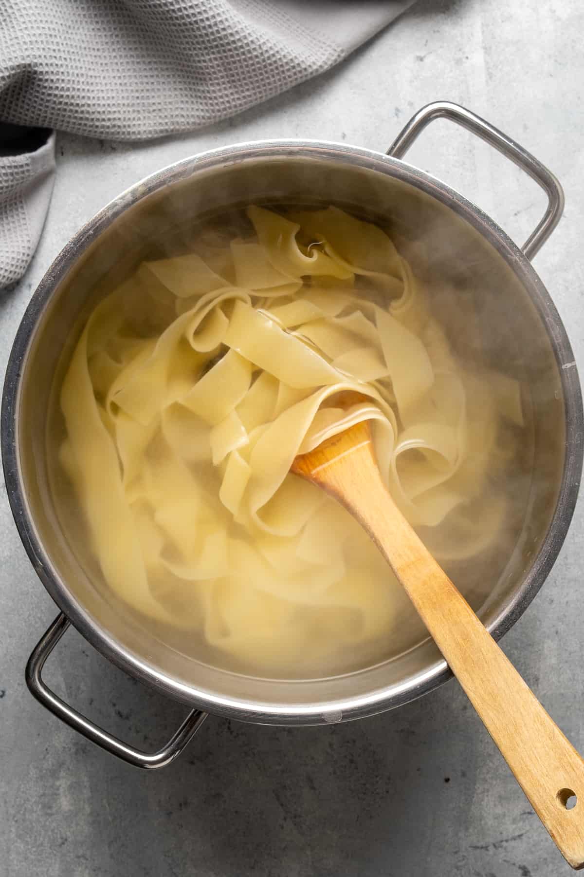 Pasta cooking in a pot and a wooden spoon in it.