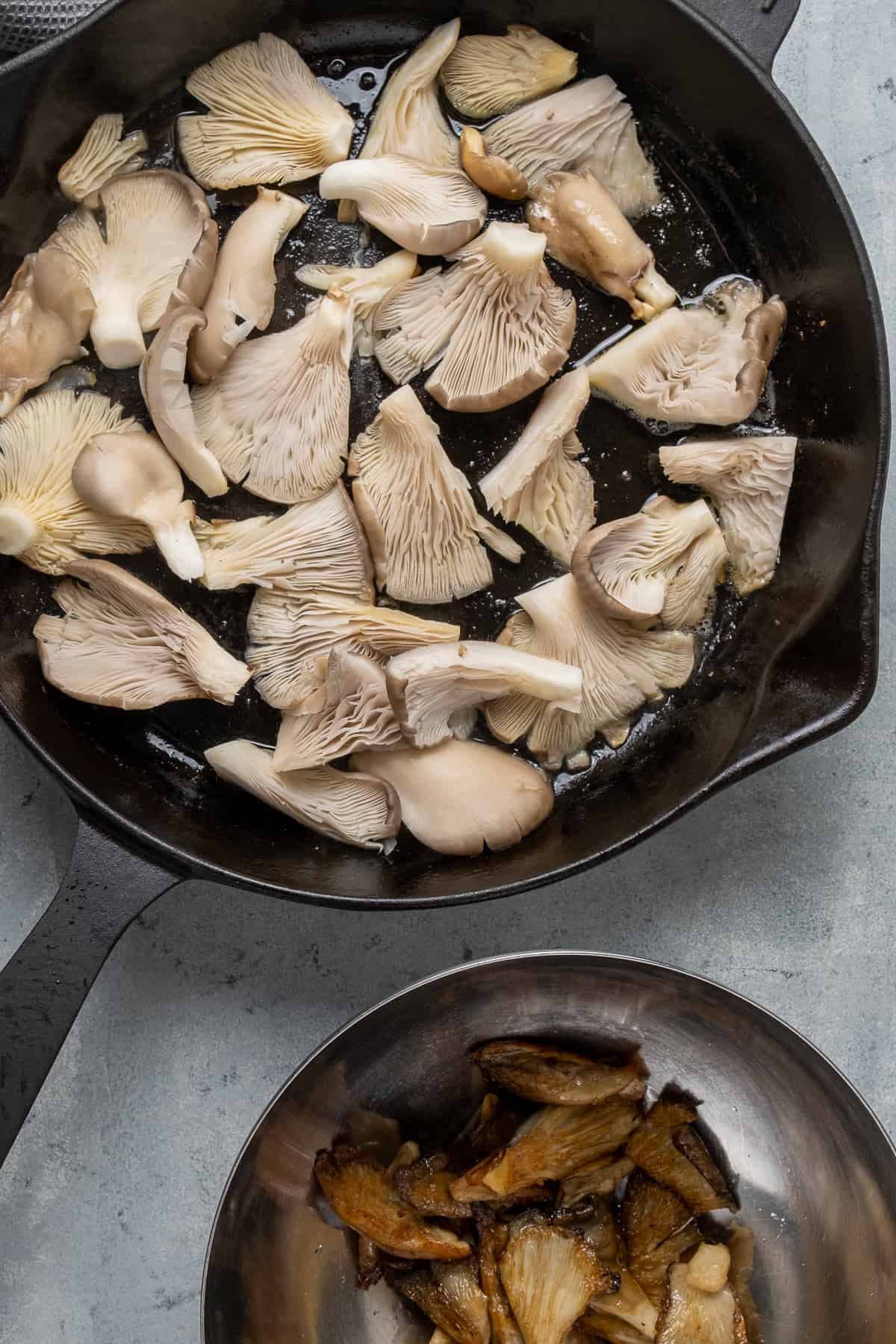 Oyster mushrooms cooking in a cast iron skillet and some fried ones are in a bowl on the side.