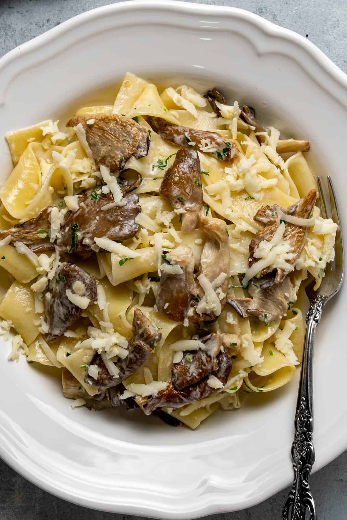 Oyster mushroom pasta topped with grated cheese in a white bowl and a fork inside it.