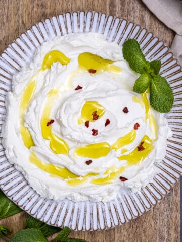 Strained yogurt drizzled with olive oil and garnished with fresh mint leaves and red pepper flakes on a white ceramic plate.
