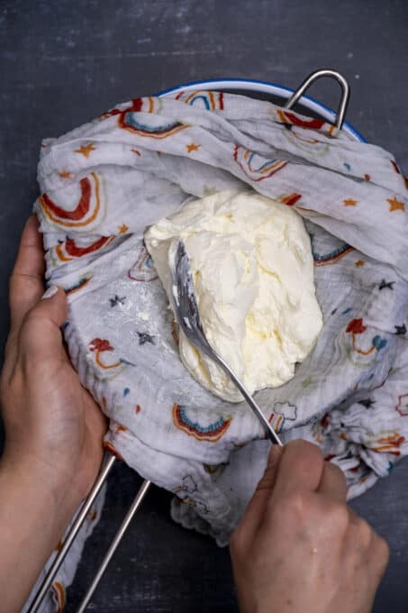 Hands checking the consistency of straining yogurt with a spoon on a baby muslin.