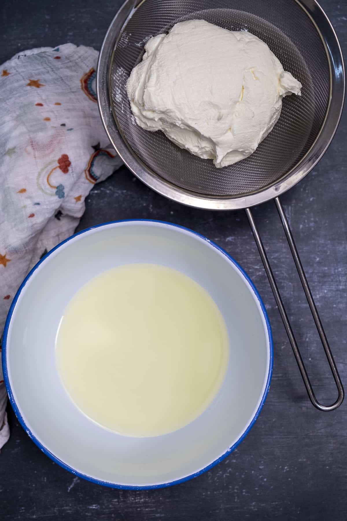 Strained yogurt on a fine strainer and the whey removed from it in a white bowl.