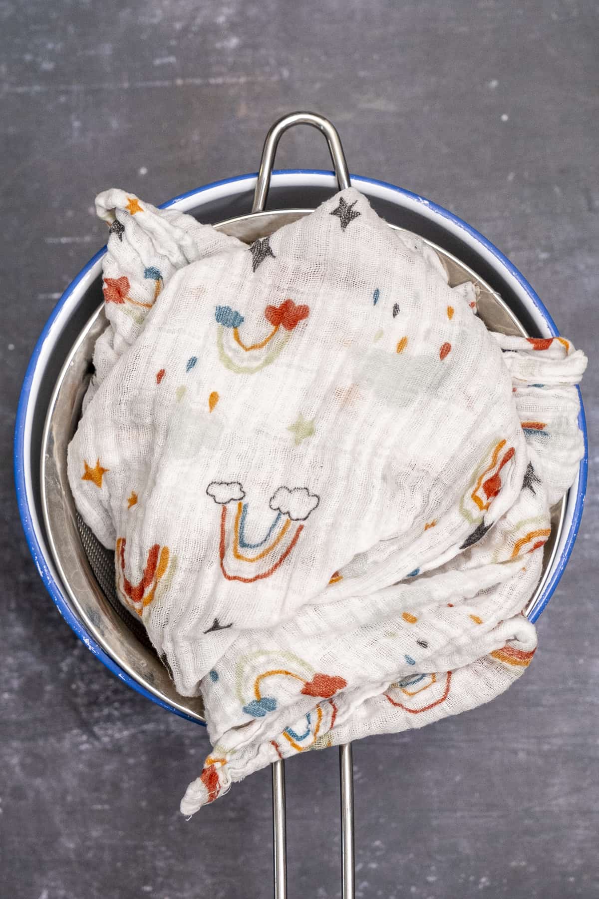 Baby muslin folded on the yogurt in a strainer over a large bowl.