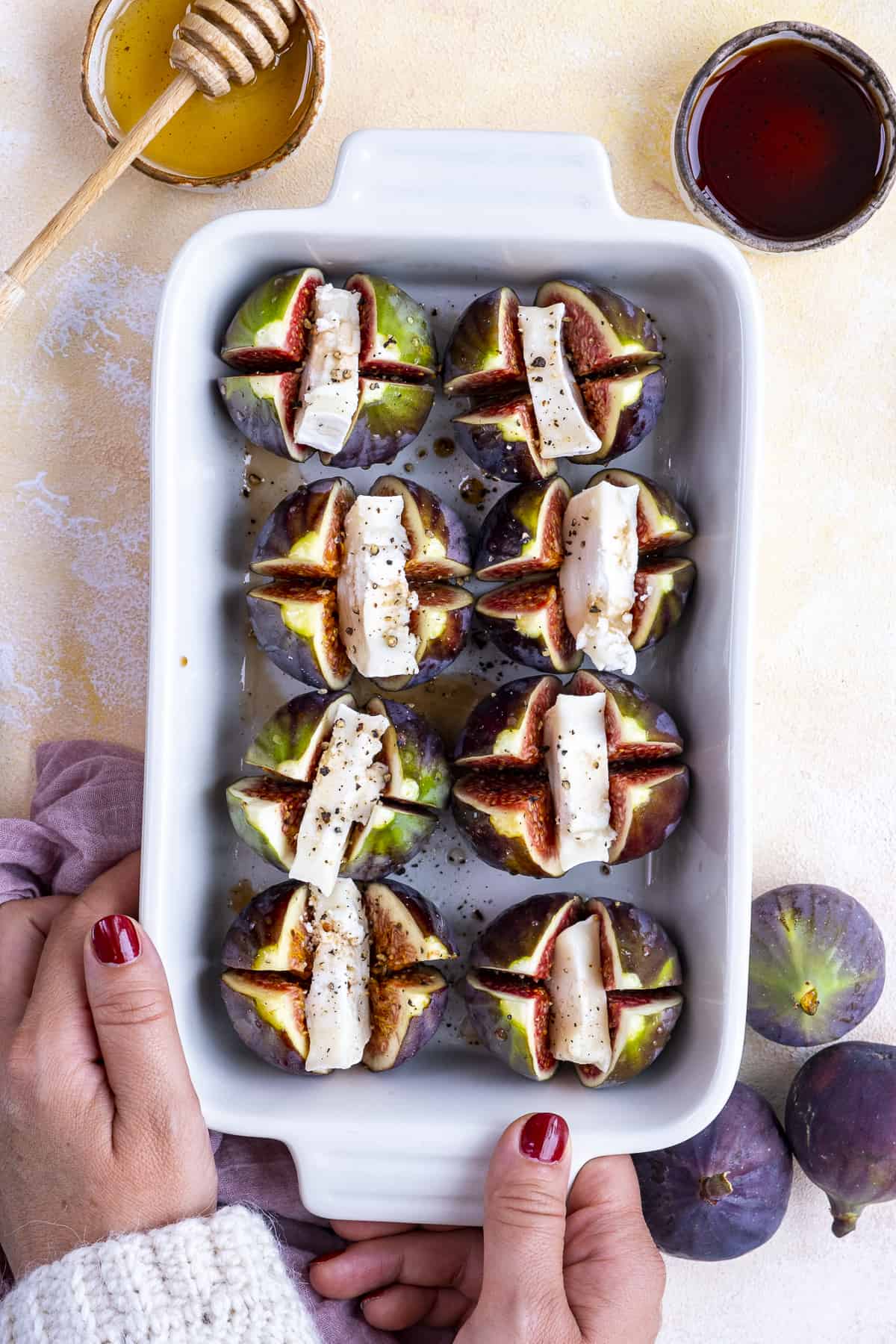 Woman hands holding a baking pan with fresh figs stuffed with cheese.