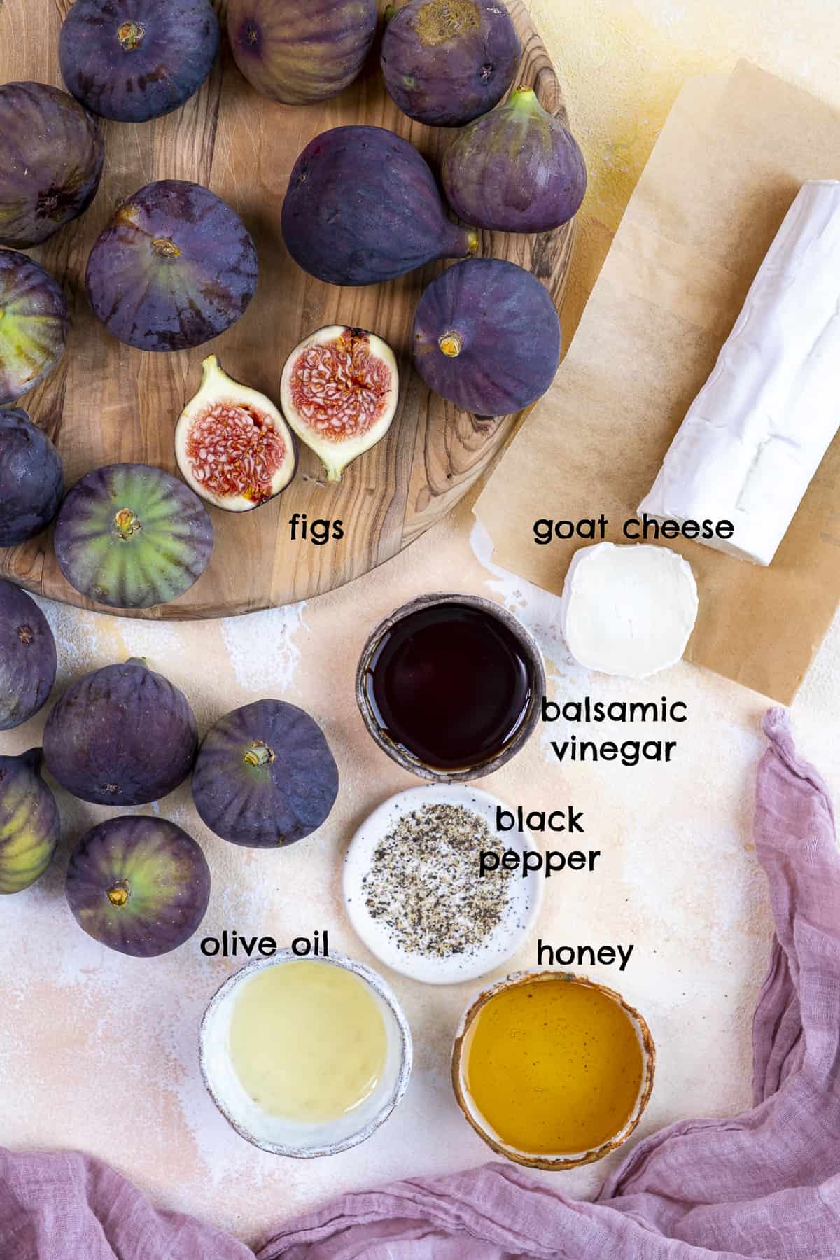 Fresh figs, goat cheese, honey, balsamic vinegar, oil and black pepper on a light background.