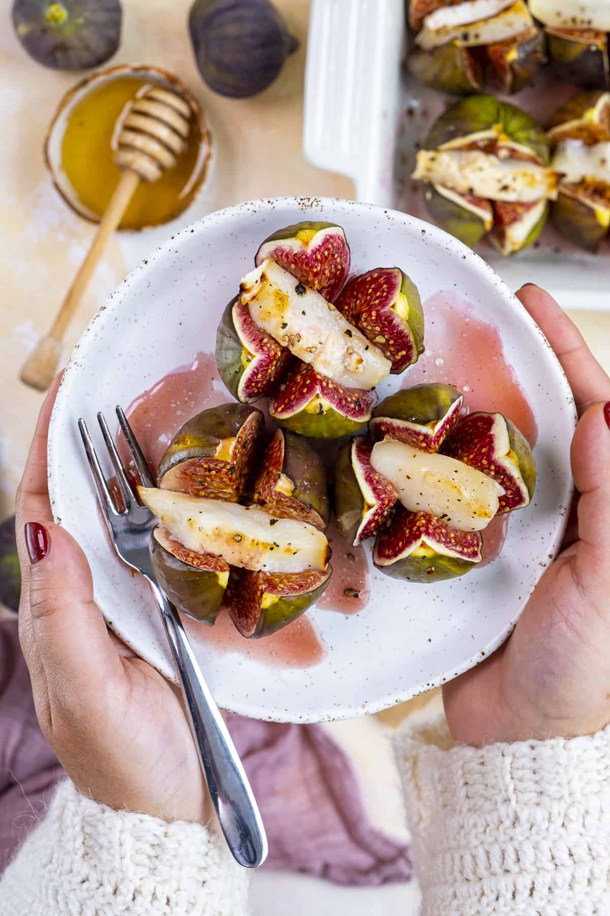 Woman hands holding a plate with baked stuffed figs.