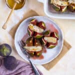 Baked stuffed figs with goat cheese on a white plate and a spoon on the side.