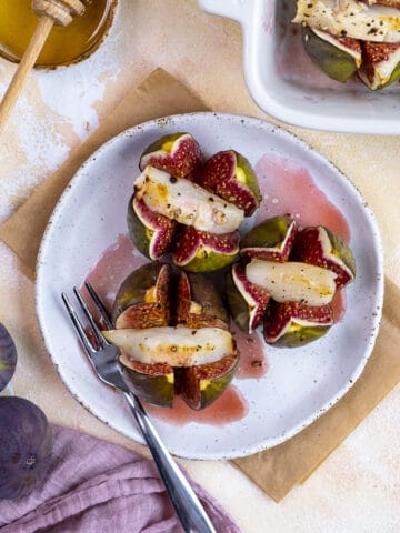 Baked stuffed figs with goat cheese on a white plate and a spoon on the side.