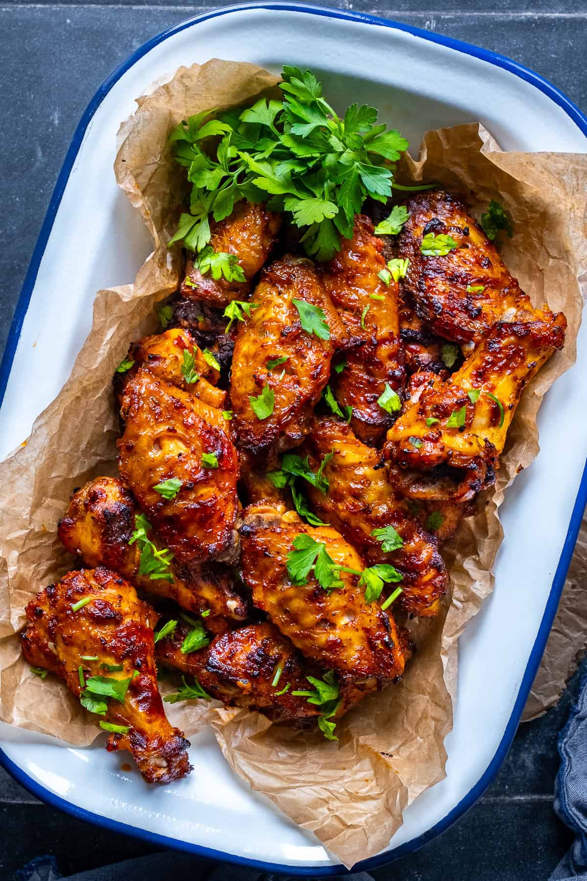Golden Turkish chicken wings topped with parsley, served on parchment in a white enamel tray.