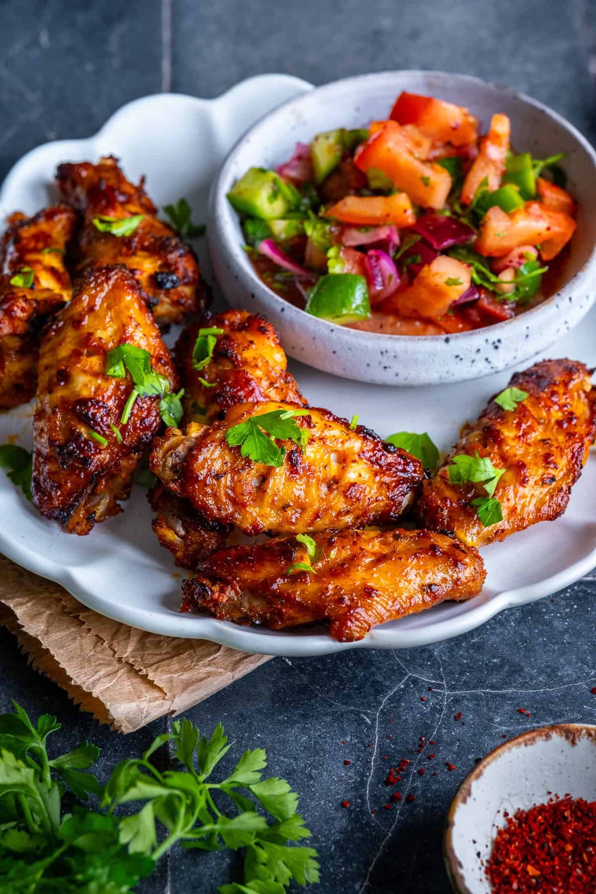 Close-up of Turkish chicken wings with parsley, served alongside a fresh tomato and cucumber salad.