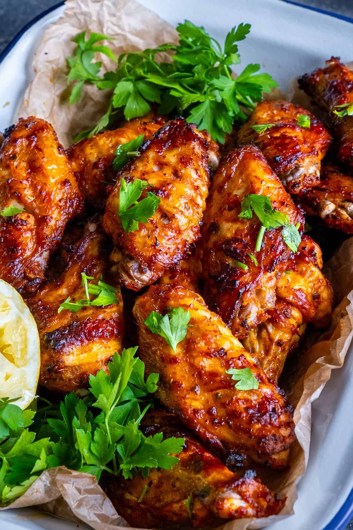 Close-up of golden Turkish chicken wings with parsley and a lemon wedge on parchment paper.